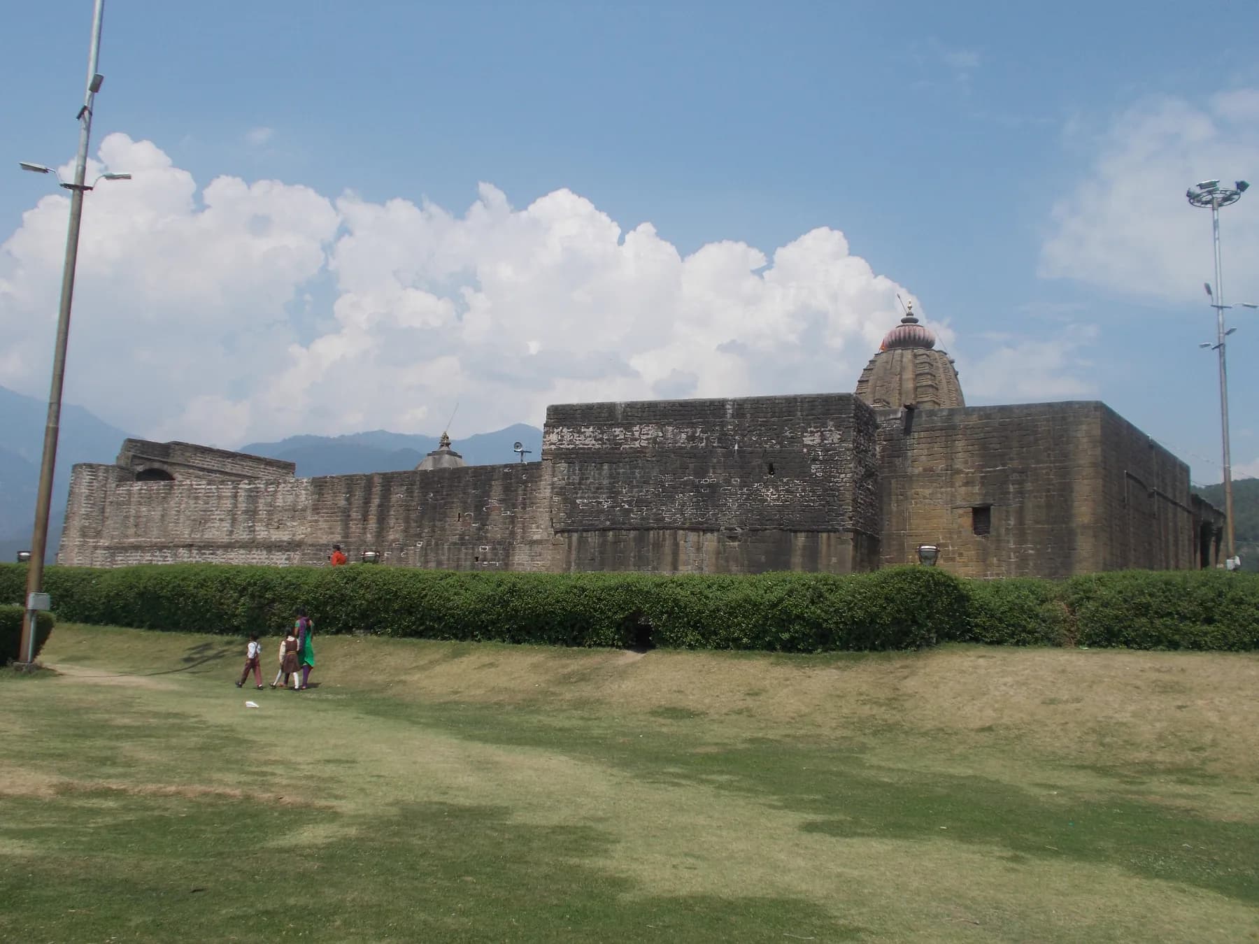 The stone enclosure and tower of Baijnath Temple in Kangra, with lawns and hills behind