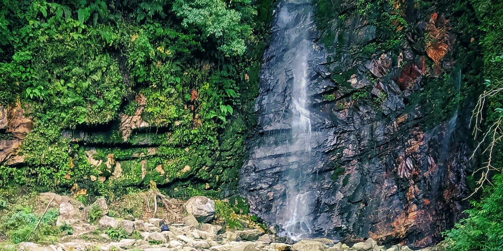 Chhoie Waterfall flowing down a layered rock face surrounded by greenery