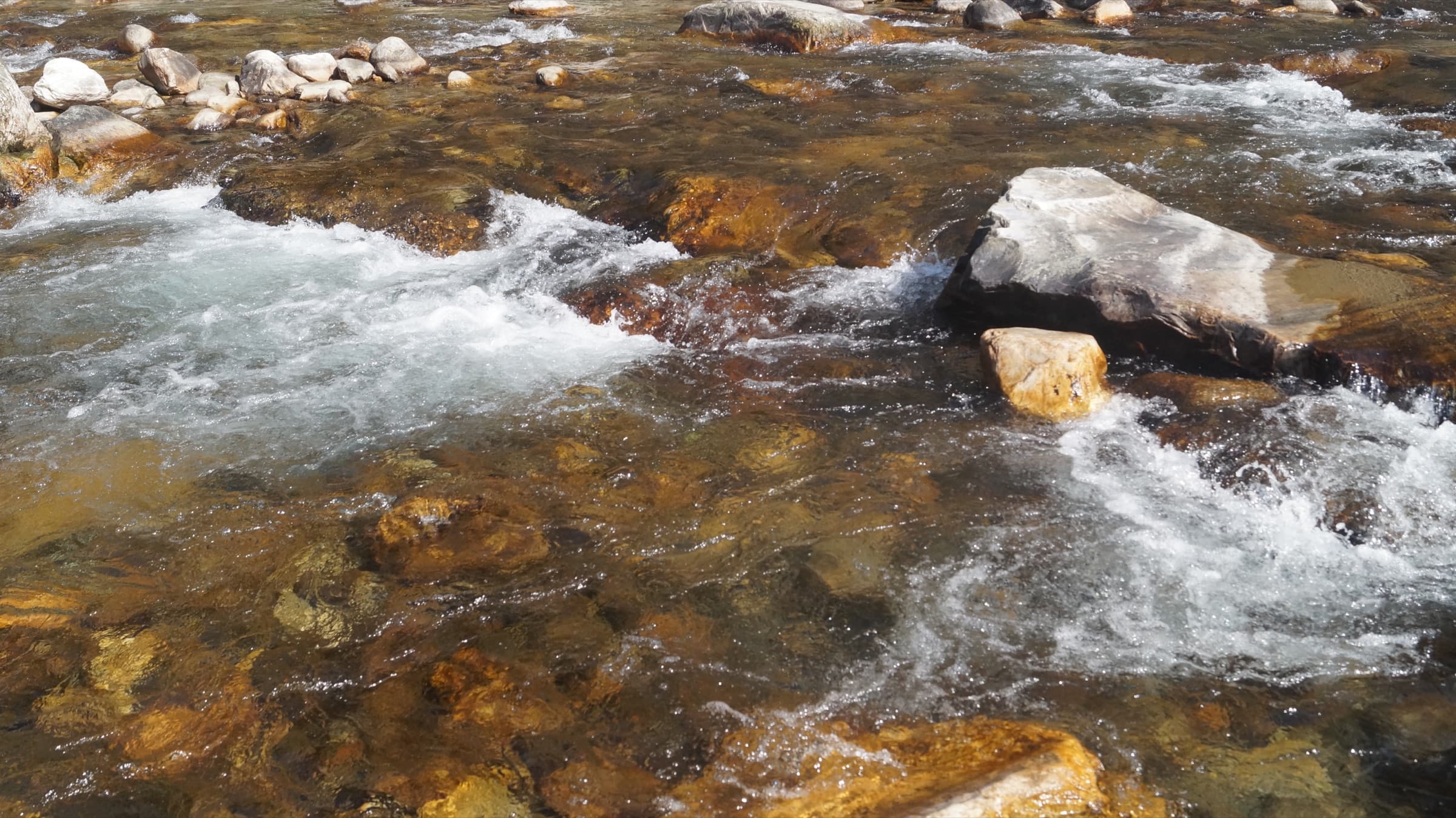 Clear water flowing around rocks in the Tirthan River