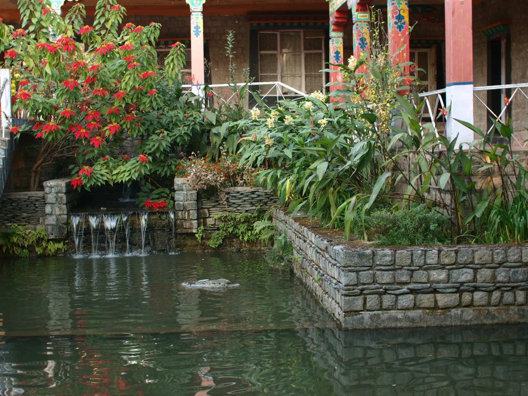 A stone-lined water garden with plants and painted columns at Norbulingka Institute