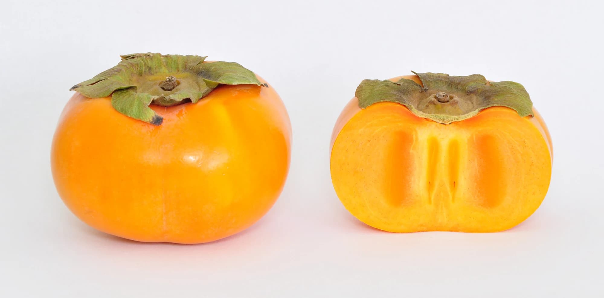 Whole and halved orange persimmons with leafy caps on a white background