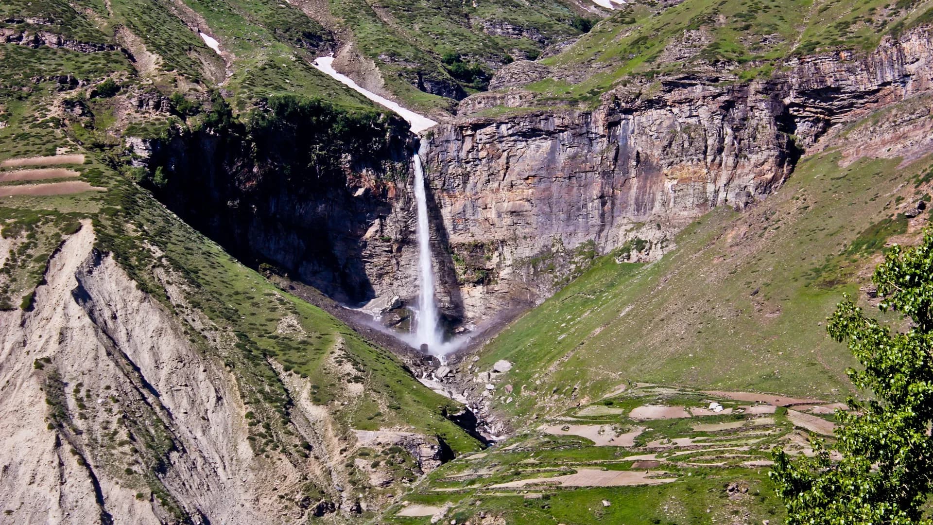 Sissu Waterfall descending through a rocky green mountainside in Lahaul